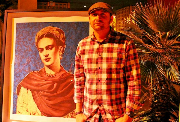 Antonio Pelayo standing in front of a painting of Frida at MOLAA